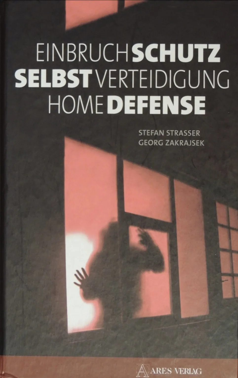 Buchcover vorne: „Einbruchschutz – Selbstverteidigung – Home Defense“ von Stefan Strasser und Georg Zakrajsek, ARES Verlag; Schatten einer Person mit erhobener Hand hinter einem rötlich beleuchteten Fenster